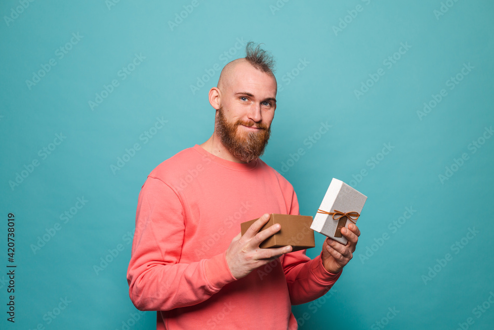 Bearded european man in casual peach isolated on turquoise background excited opening gift box Bearded european man in casual peach isolated on turquoise background excited opening gift box