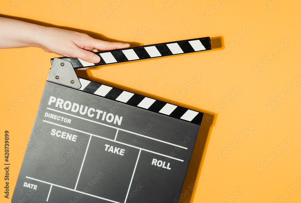 Hand holding film clapperboard on yellow studio background