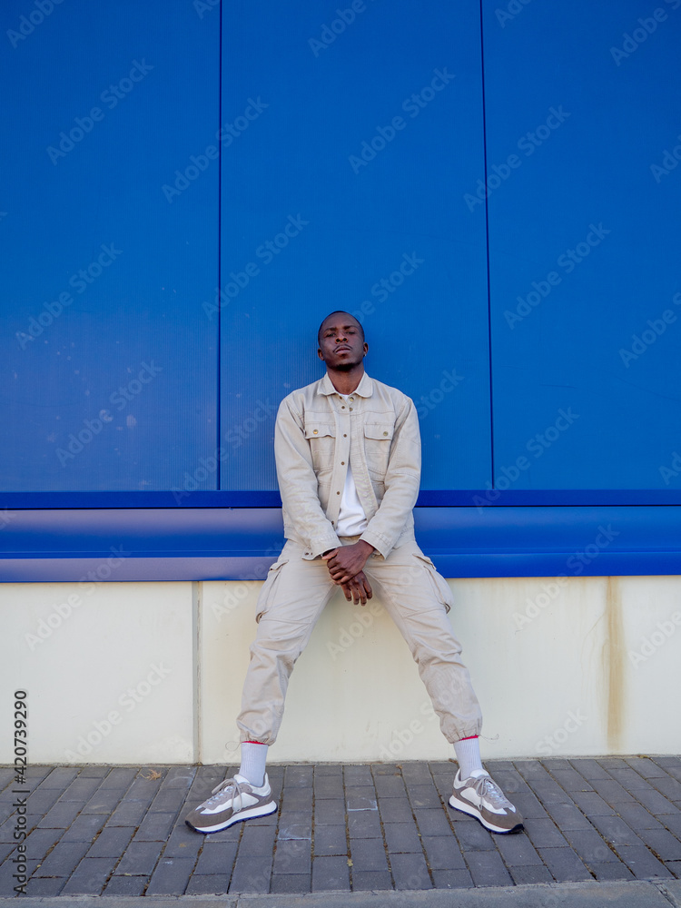 Hombre negro sentado y apoyado en una pared azul