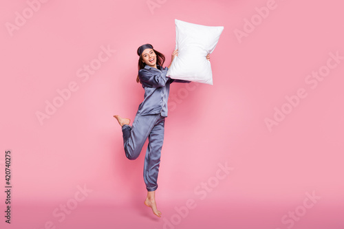 Full length body size photo of girl in sleepwear laughing fighting with pillow on pajama party isolated on pastel pink color background