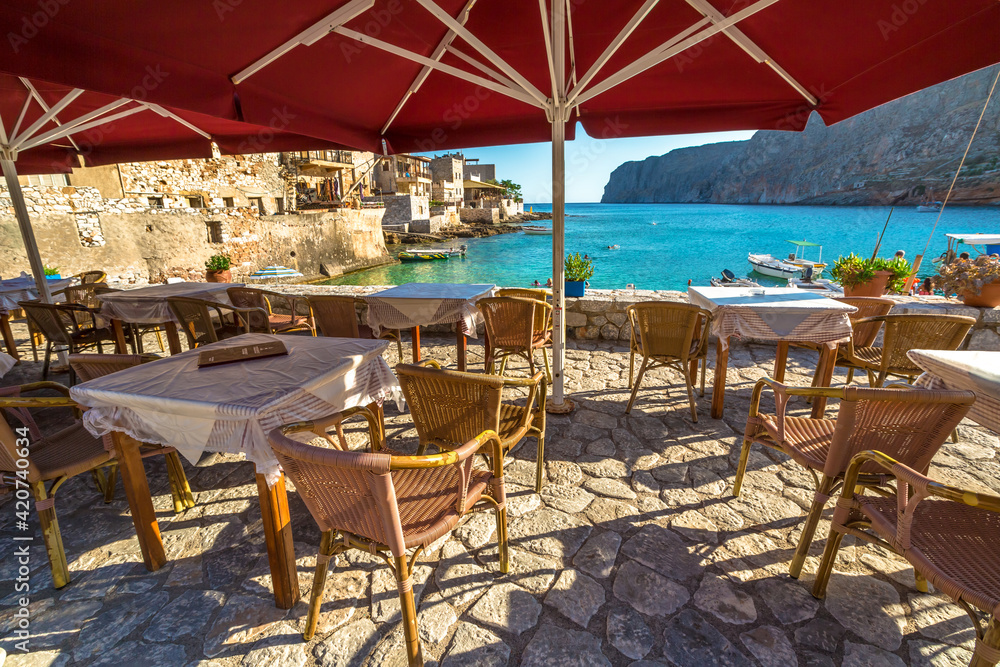 Gerolimenas village, Mania Peninsula, Lakonia, Peloponnese, Greece - August 23, 2015: Typical tavern greek on waterfront between mountains and bay with tropical waters, stone beach and fishing boats.