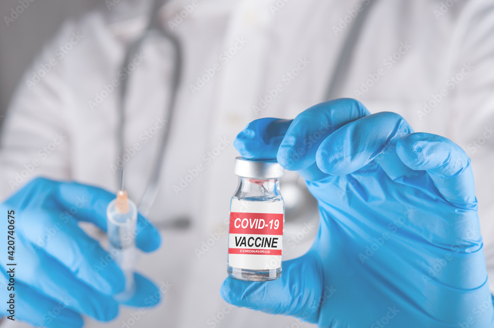 doctor with stethoscope on the neck and hand in medical glove holding syringe and vial of the coronavirus vaccine for injection. preventing spread of covid-19 concept. closed up and selective focus doctor with stethoscope on the neck and hand in medical glove holding syringe and vial of the coronavirus vaccine for injection. preventing spread of covid-19 concept. closed up and selective focus