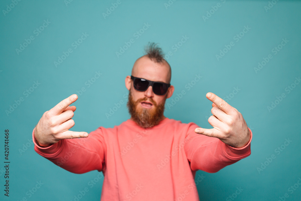 Fototapeta premium Bearded european man in casual peach isolated on turquoise background shouting with crazy expression doing rock symbol with hands up