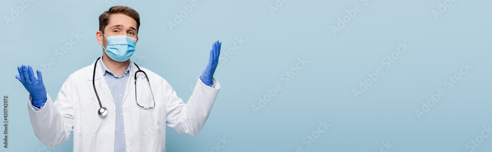young doctor in medical mask and white coat standing with outstretched hands isolated on blue, banner young doctor in medical mask and white coat standing with outstretched hands isolated on blue, banner