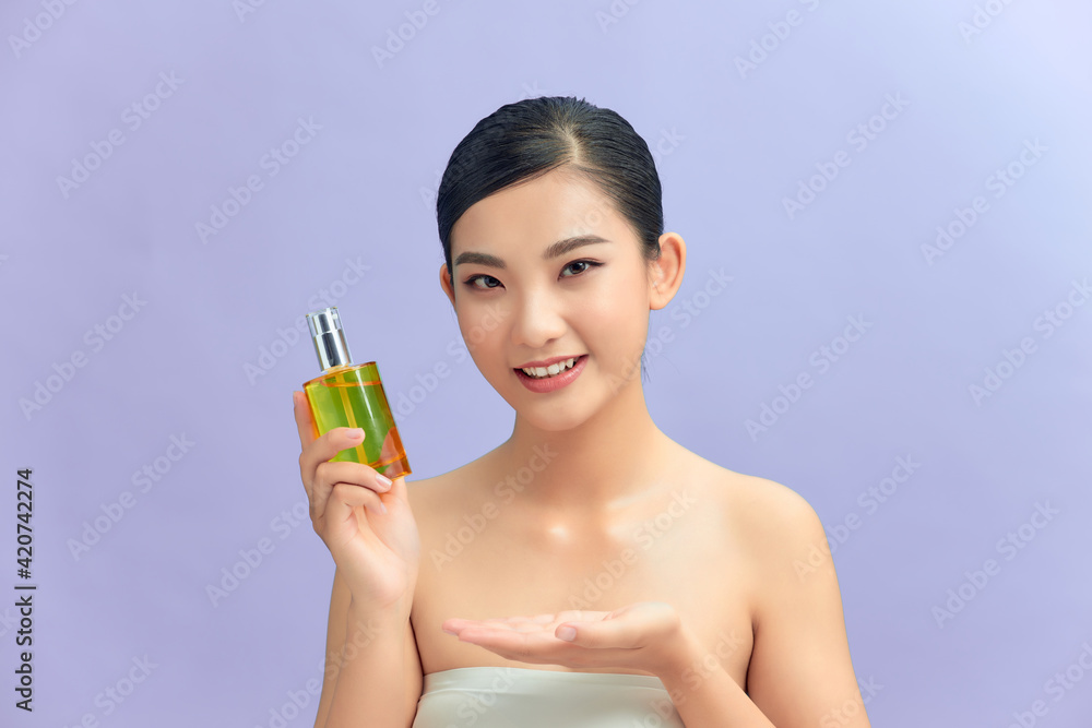 Beauty portrait of an attractive happy healthy topless brunette woman isolated over purple background, showing cosmetic bottle Beauty portrait of an attractive happy healthy topless brunette woman isolated over purple background, showing cosmetic bottle