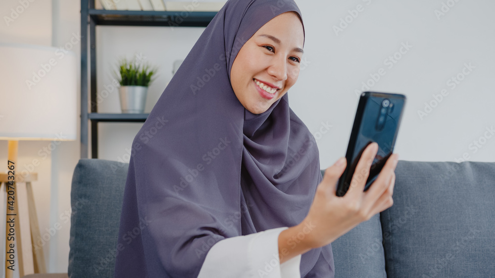 Asia muslim lady wear hijab using phone video call talking with couple at home. Young teenager making vlog video to social media on sofa in living room. Social distancing, quarantine for corona virus. Asia muslim lady wear hijab using phone video call talking with couple at home. Young teenager making vlog video to social media on sofa in living room. Social distancing, quarantine for corona virus.