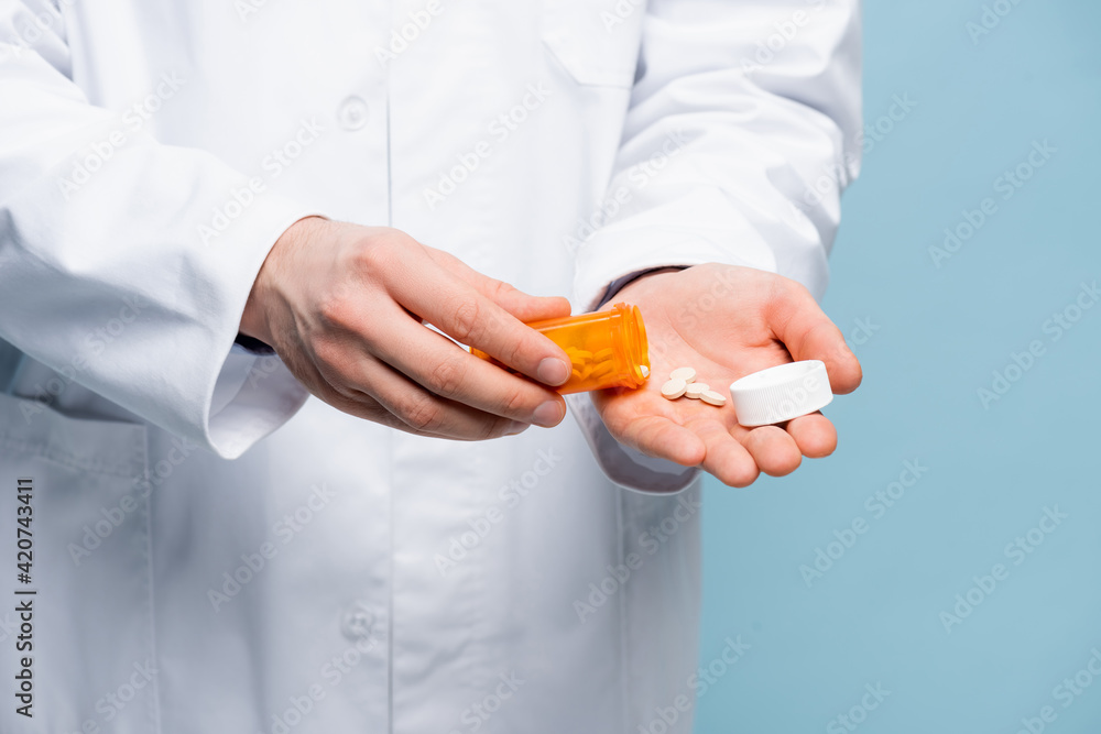 cropped view of doctor in white coat holding pills and bottle in hands isolated on blue cropped view of doctor in white coat holding pills and bottle in hands isolated on blue