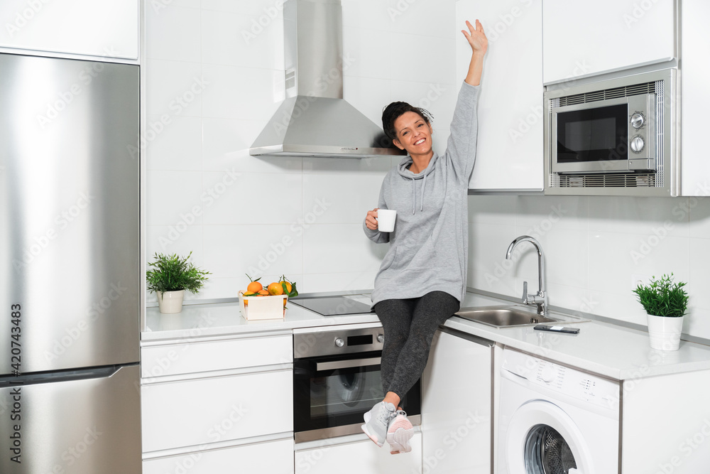 smiling woman with braids, sitting in the kitchen with a white mug in her hand, oranges and plants around, dressed in gray sweatshirt. lifestyle and kitchen smiling woman with braids, sitting in the kitchen with a white mug in her hand, oranges and plants around, dressed in gray sweatshirt. lifestyle and kitchen