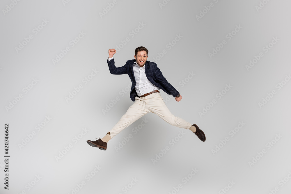 full length of happy young man with clenched fists levitating on grey