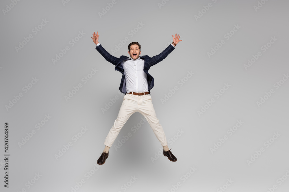 full length of excited man with outstretched hands levitating on grey