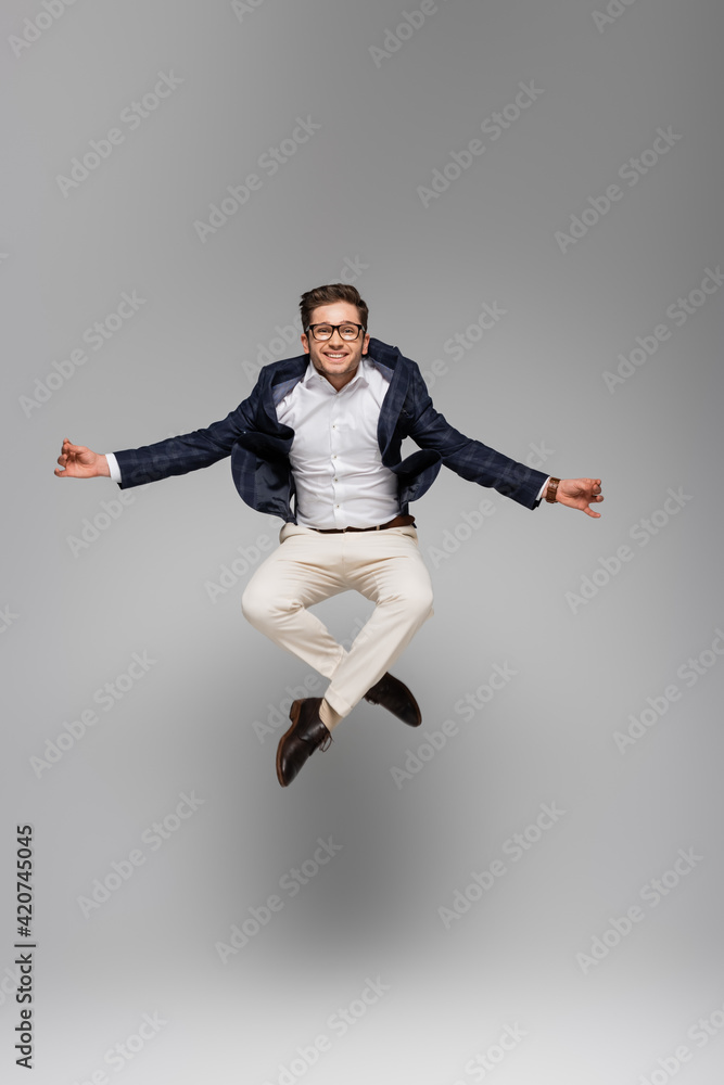 full length of cheerful businessman in glasses meditating and levitating on grey