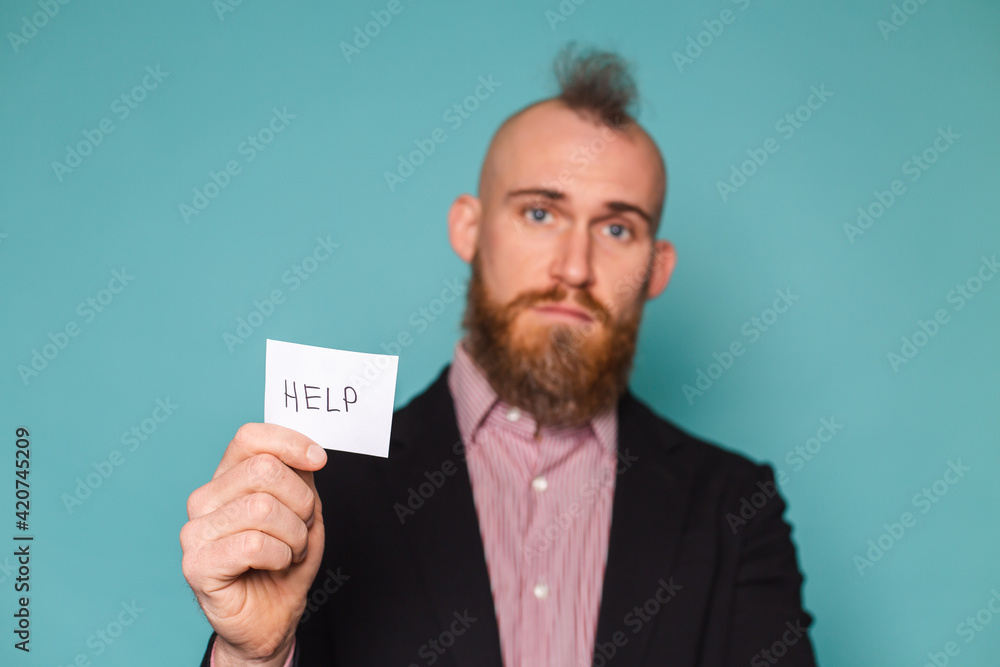 Bearded european businessman in dark suit isolated on turquoise background holding paper with help sign sad unhappy begs Bearded european businessman in dark suit isolated on turquoise background holding paper with help sign sad unhappy begs