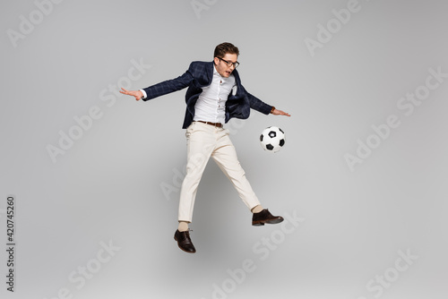 full length of cheerful businessman playing football while levitating on grey
