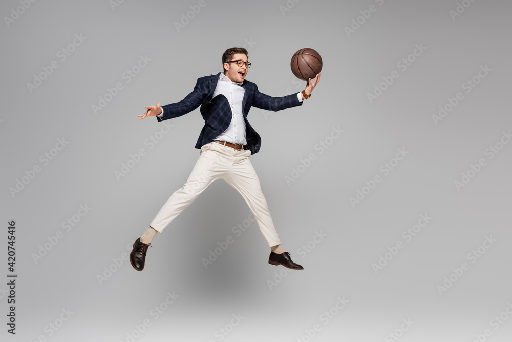 full length of cheerful man in glasses playing basketball and levitating on grey full length of cheerful man in glasses playing basketball and levitating on grey