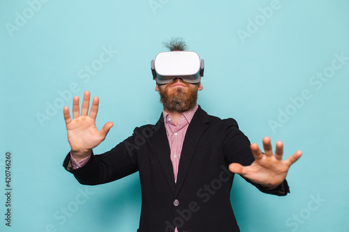 Bearded european businessman in dark suit isolated on turquoise background excited amazed touch air wearing virtual reality glasses