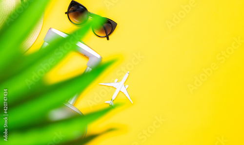 Sea background. Travel accessories with suitcase, white plane, palm leaves in minimal trip vacation concept on yellow background. Tranquil beach scene with copy space.