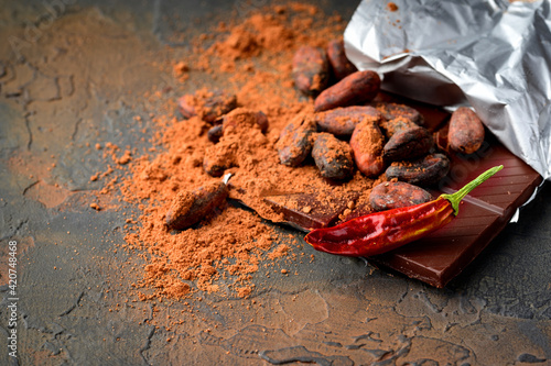 Dark chocolate, red chilli peppers, cocoa beans and powder on a dark stone background. © Bera_berc
