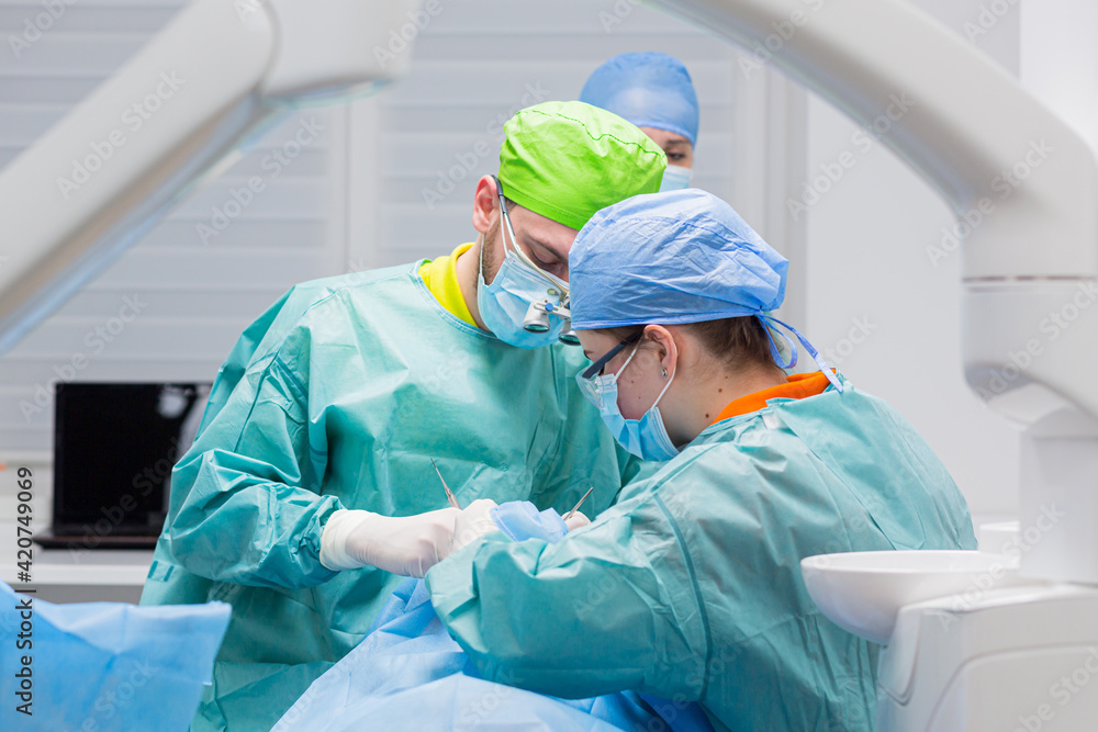 Team of dental surgeons performs surgery on teeth. in a modern clinic. Young dentist. Teamwork. Tooth doctor orthodontist surgeon doing medical operation on root canals. Stomatology office.
Team of dental surgeons performs surgery on teeth. in a modern clinic. Young dentist. Teamwork. Tooth doctor orthodontist surgeon doing medical operation on root canals. Stomatology office.