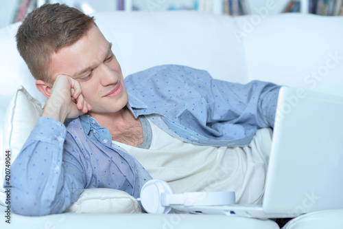 handsome young man lying on white couch with laptop