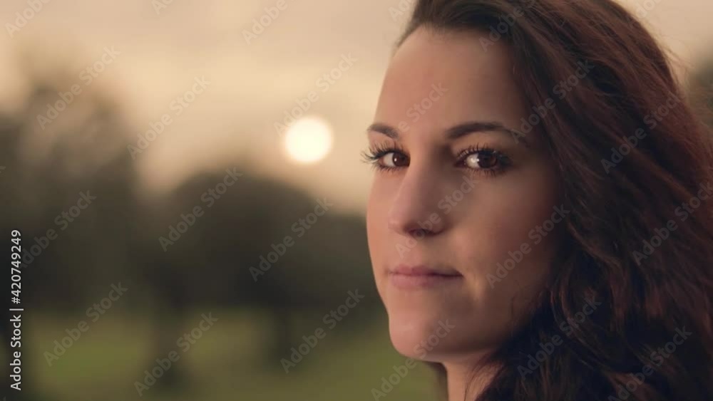 Mujer joven con chaqueta roja posando con el sol detrás en un prado verde con olivos y flores amarillas con el atardecer de fondo Mujer joven con chaqueta roja posando con el sol detrás en un prado verde con olivos y flores amarillas con el atardecer de fondo