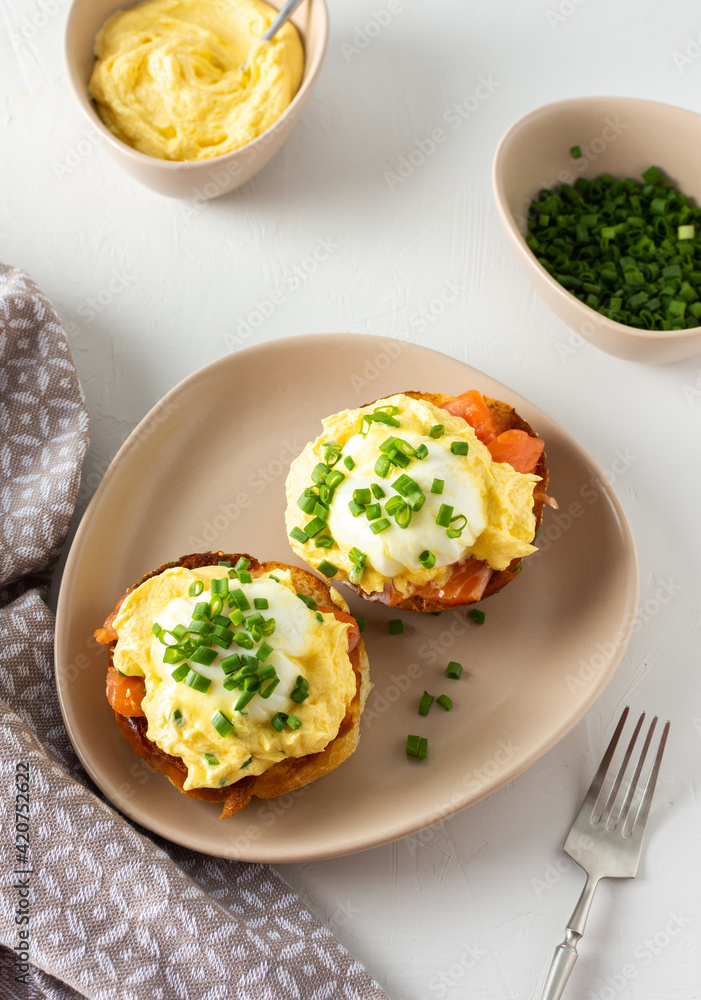 Delicious hearty breakfast, eggs Atlantic in a plate on a white background, round fried bun with salmon and eggs Benedict, hollandaise sauce and green onions