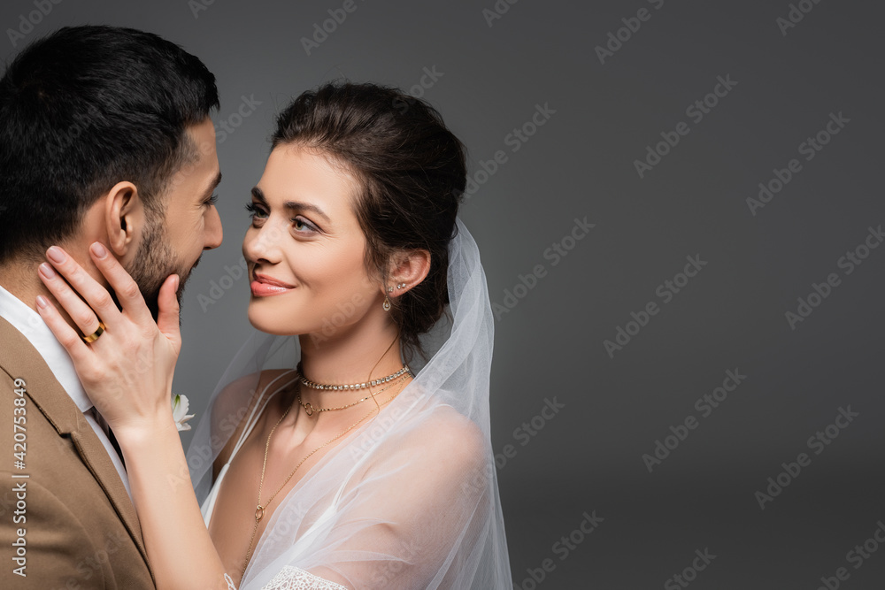 happy, elegant bride touching face of muslim fiance isolated on grey happy, elegant bride touching face of muslim fiance isolated on grey