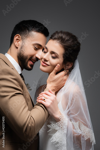 happy arabian man hugging neck of pretty, smiling bride isolated on grey