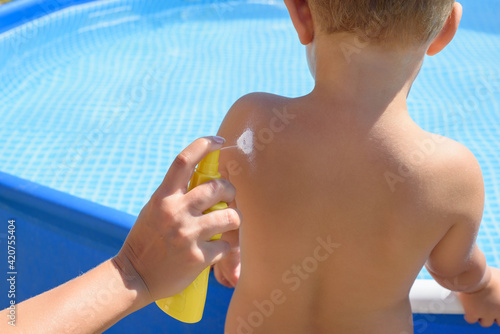 Mother puts cream on her son on the swimming pool background. Caring for baby skin.