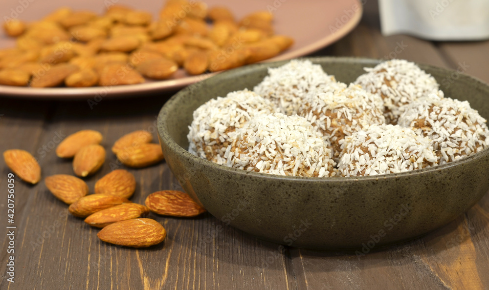 Marzipan candy being covered with grated coconut on wooden background. Round white candy with coconut flakes. Homemade snacks. Healthy food for weekdays and holidays Marzipan candy being covered with grated coconut on wooden background. Round white candy with coconut flakes. Homemade snacks. Healthy food for weekdays and holidays