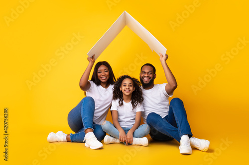 Black parents sitting under cardboard roof above daughter © Prostock-studio