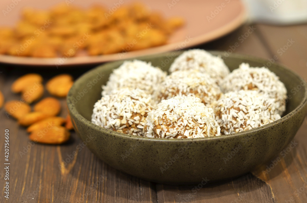 Marzipan candy being covered with grated coconut on wooden background. Round white candy with coconut flakes. Homemade snacks. Healthy food for weekdays and holidays Marzipan candy being covered with grated coconut on wooden background. Round white candy with coconut flakes. Homemade snacks. Healthy food for weekdays and holidays
