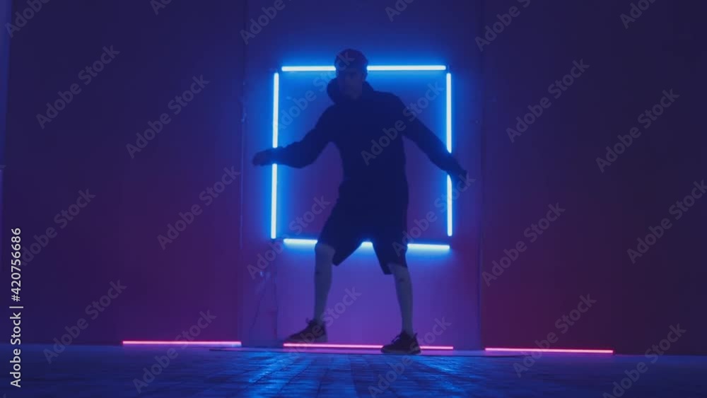 Person in windbreaker and red cap dancing to breakdance. blue rectangle neon background . Flickering neon background . man dancing to breakdance in night club Person in windbreaker and red cap dancing to breakdance. blue rectangle neon background . Flickering neon background . man dancing to breakdance in night club