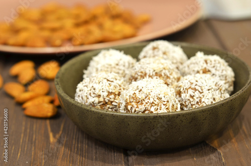 Marzipan candy being covered with grated coconut on wooden background. Round white candy with coconut flakes. Homemade snacks. Healthy food for weekdays and holidays