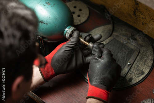 man wearing protective gloves polishes a silver ring with a grinder