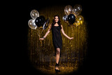 Full size photo of brown optimistic lady stand with balloons wear black dress shoes isolated on dark gold color background in stage light spot