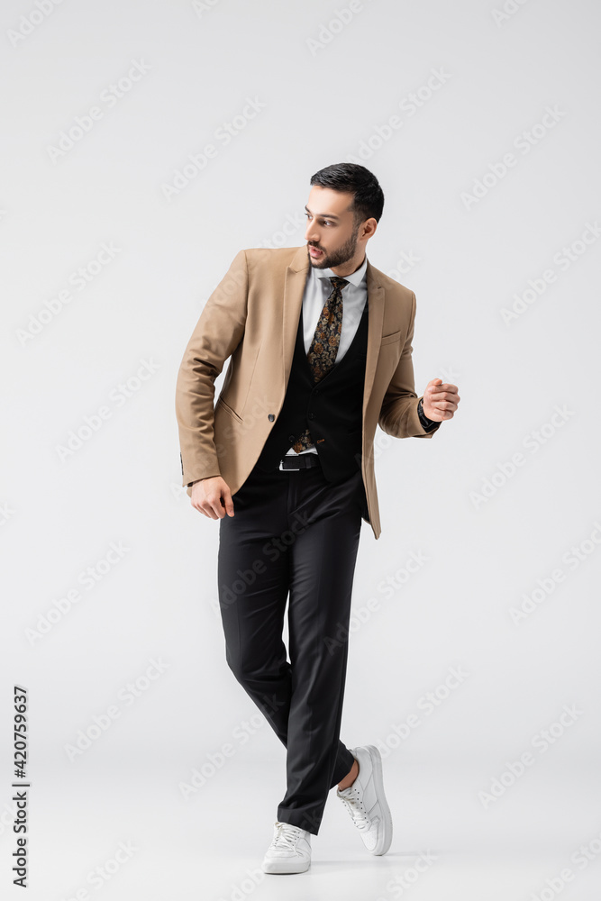 full length view of young muslim man in trendy clothes looking away on grey full length view of young muslim man in trendy clothes looking away on grey