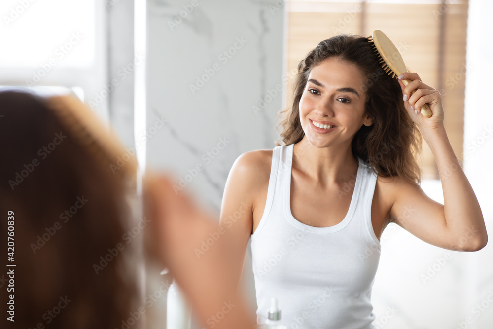 Cheerful Female Combing And Brushing Her Wavy Hair In Bathroom Cheerful Female Combing And Brushing Her Wavy Hair In Bathroom