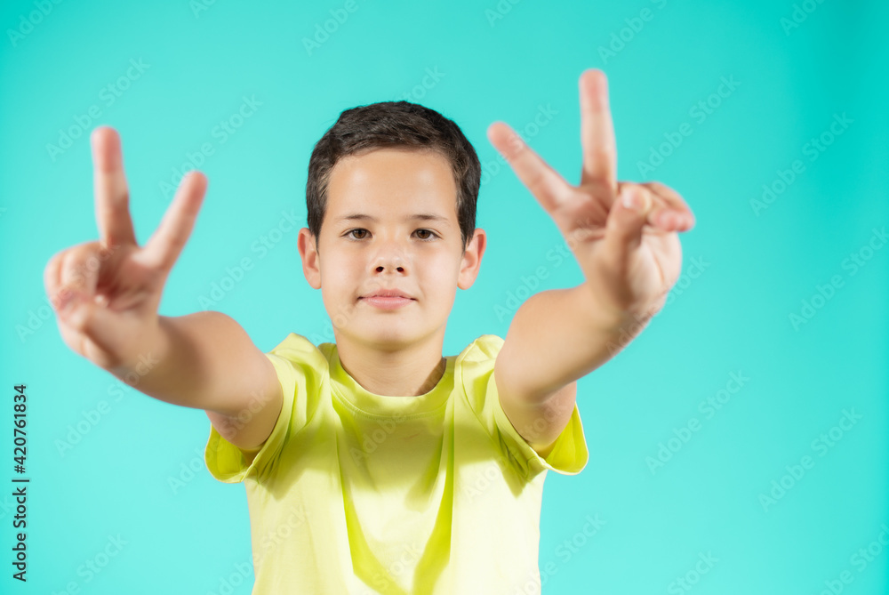 Portrait of little boy showing victory hands sign on green background Portrait of little boy showing victory hands sign on green background