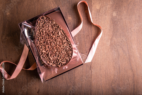 Canvas Print Top view of stuffed chocolate easter egg with a spoon with an untied gift bow in a transparent pack on a wooden table