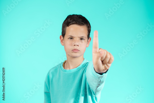 Portrait of cheerful boy with good idea - isolated over green background. 10 year old kid pointing finger up. Child points by finger upward. Cheerful boy shows something