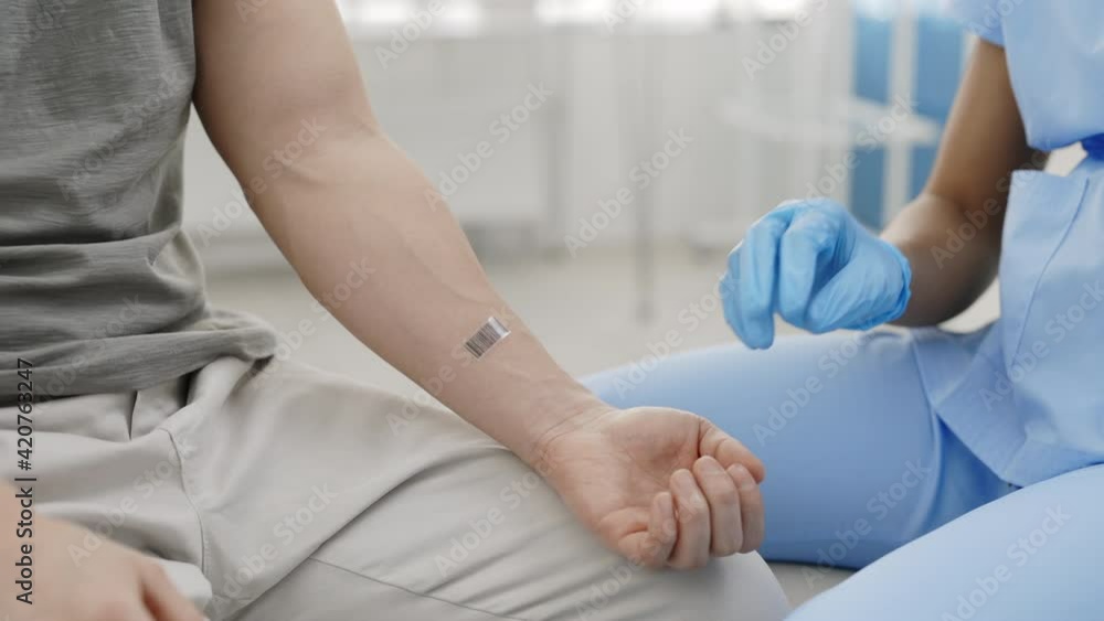 Crop view of female doctor in protective medical gloves and mask scanning bar code on male patient arm before giving shot of vaccine in his shoulder. Concept of vaccination program. Crop view of female doctor in protective medical gloves and mask scanning bar code on male patient arm before giving shot of vaccine in his shoulder. Concept of vaccination program.