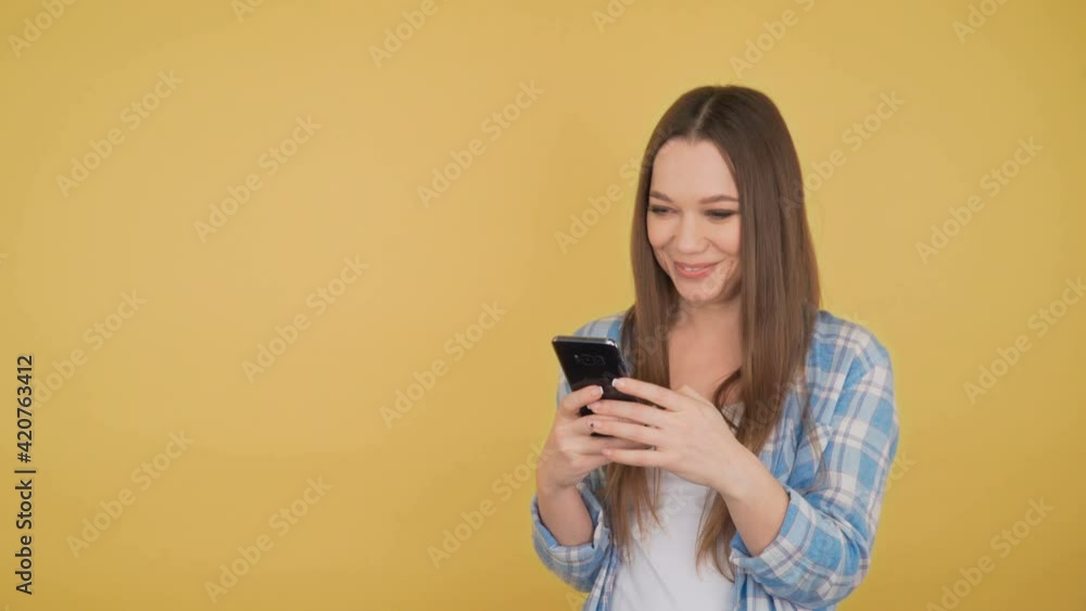 smiling young woman student on yellow background looking looks at smartphone smiling young woman student on yellow background looking looks at smartphone