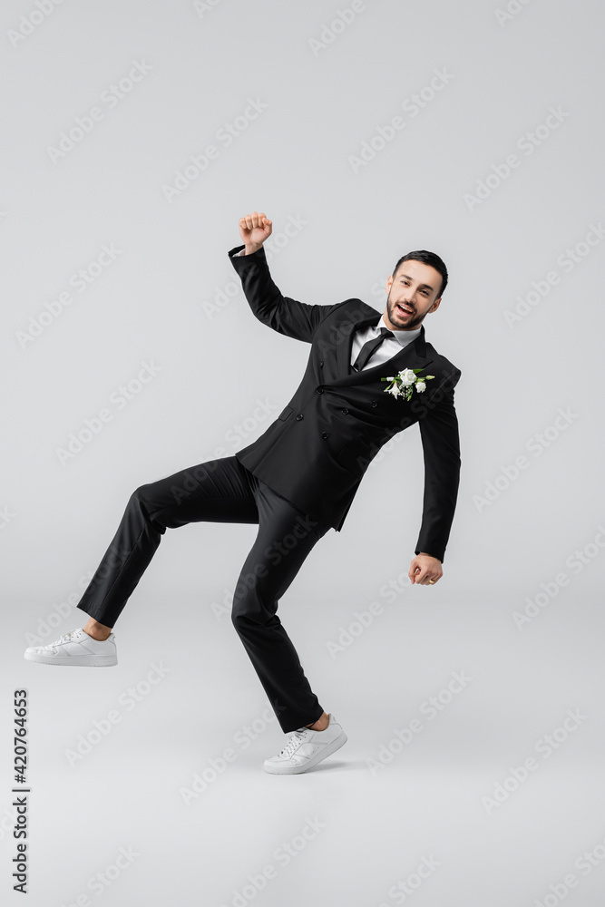 Excited arabian groom showing yes gesture while jumping on grey background