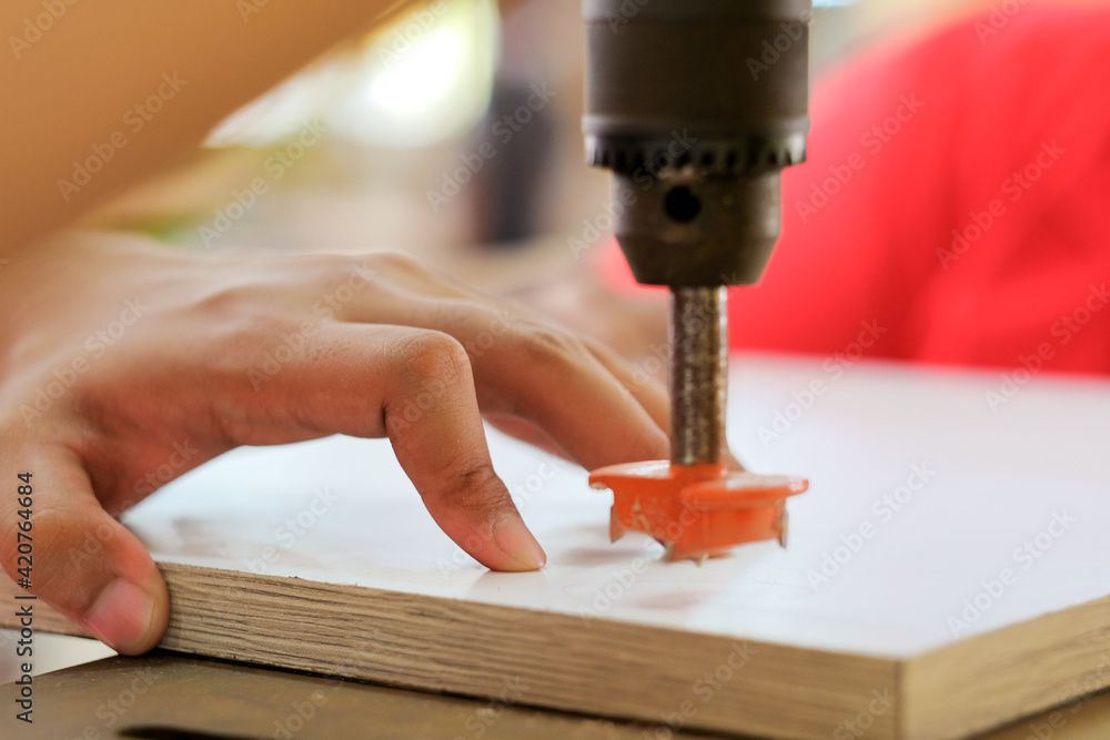 The carpenter is using a bench drill to fasten the hinge screws on to the wooden door.. The carpenter is using a bench drill to fasten the hinge screws on to the wooden door..