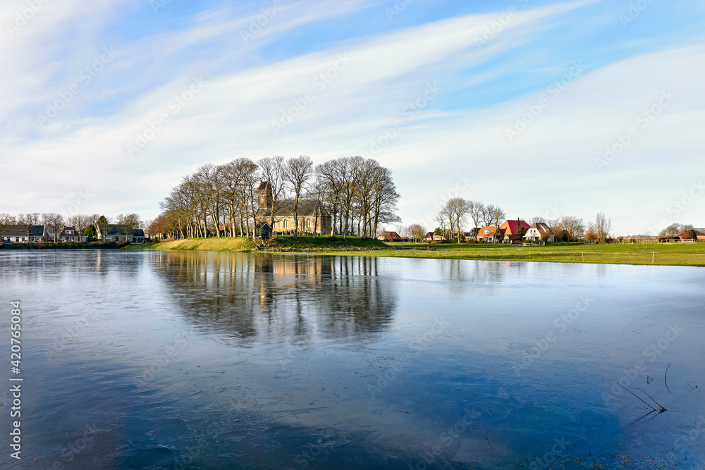 The 12th century romanesque Saint Nicholas Church on mound in Hijum Friesland with outdoor ice-skating rink in front during winter. The 12th century romanesque Saint Nicholas Church on mound in Hijum Friesland with outdoor ice-skating rink in front during winter.