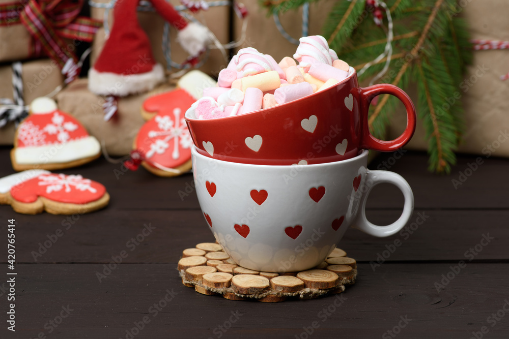 red ceramic cup with cocoa and marshmallows, behind a gift box and a Christmas garland