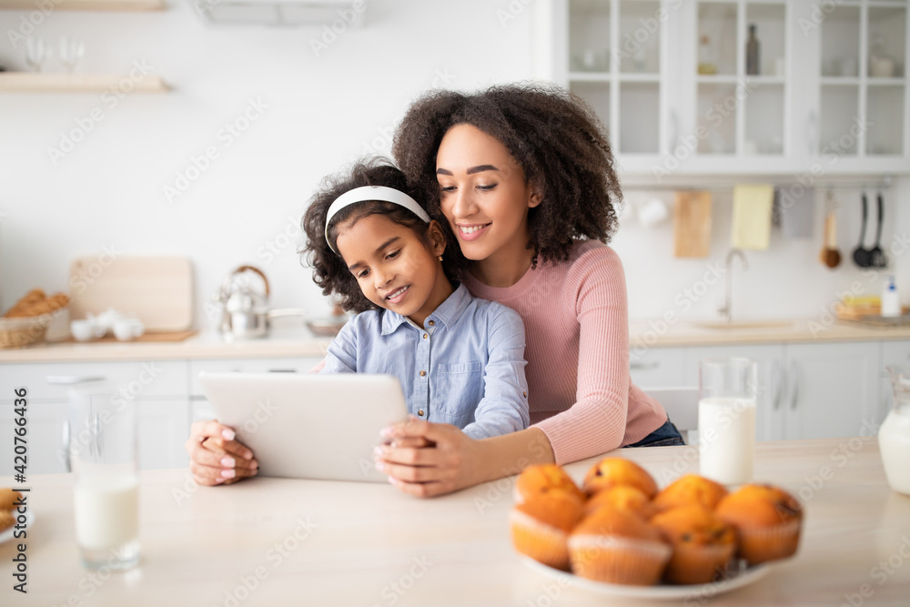 Black woman and girl using tablet in kitchen