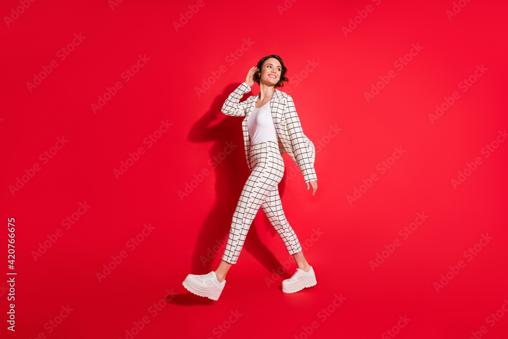 Full size profile side photo of young attractive woman happy smile look empty space go walk isolated over red color background Full size profile side photo of young attractive woman happy smile look empty space go walk isolated over red color background