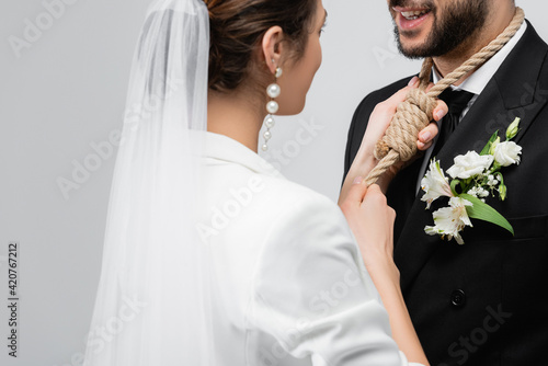 Young bride wearing slip knot on neck of groom isolated on grey photo