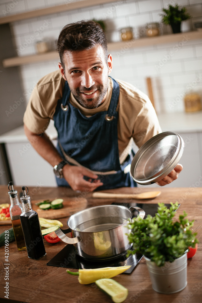 Happy smiling man preparing tasty meal. Young man cooking in the kitchen.. Happy smiling man preparing tasty meal. Young man cooking in the kitchen..